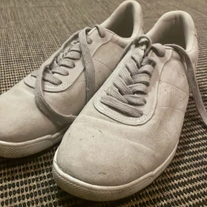 Grå sneakers från H&M, storlek 39 - Säljer ett par stilrena grå sneakers från H&M i storlek 39. Skorna har klassisk design med rund tå, platt sula och snörning. Ovandelen är i mjuk mockaimitation och insidan är fodrad med textil för extra komfort. Perfekta för en clean och enkel look.