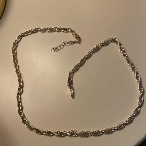Silverfärgat tvinnat halsband - Snyggt halsband i silverfärgad metall med tvinnad kedja och justerbar längd. Perfekt för dig som gillar stilrena och klassiska smycken med lite extra detalj. Låset är enkelt att använda och kedjan har en cool, flätad look.