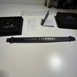 Mörk och ljus blå armband från Armani Exchange - Stilrent armband från Armani Exchange med två olika färger. Armbandet  har en klassisk rak form och justerbara hål för perfekt passform. Kommer med originalförpackning, tygpåse och äkthetscertifikat. Perfekt för dig som gillar exklusiva accessoarer. Jag har 17cm omkrets på min handled och den passar perfekt på mig om man späner den till det sista hålet