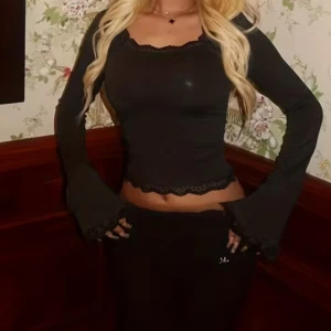 Svart långärmad topp - Säljer en svart topp med långa ärmar och snygga volangdetaljer vid ärmslut och nederkant. Toppen har en feminin v-ringad hals och är figurnära med spetskant som ger en extra touch. Perfekt för dig som gillar trendiga och stilrena plagg.