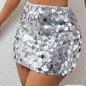 Silvrig paljettkjol med kort passform - Glittrande silvrig minikjol täckt med stora paljetter som reflekterar ljuset. Kjolen har en tight och kort passform som framhäver benen och ger en festlig vibe. Perfekt för att sticka ut på dansgolvet eller när du vill ha extra bling.