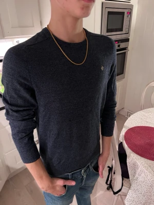 Mörkblå stickad tröja med emblem - Snygg mörkblå stickad tröja från Morris med diskret emblem på bröstet. Tröjan har rund hals, ribbade muddar och lång ärm. Perfekt till jeans och passar dig som gillar stilren design med en liten detalj. Den passar S men sitter lite som xs för dig som är noggrann 😊