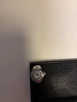 Silver klockring med vit urtavla - En silverfärgad ring med inbyggd klocka. Passar till alla tillfällen, stilren och oanvänd. Justerbar storlek.