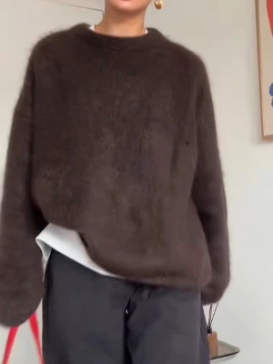 Mörkbrun stickad tröja från & Other Stories - Mysig mörkbrun stickad tröja från & Other Stories med rund hals och långärmad passform. Tröjan har en loose fit och är tillverkad i ett fluffigt material som ger en skön och avslappnad vibe. Perfekt att slänga på sig när det är kyligt ute.