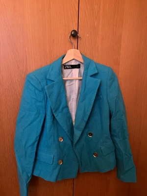 Turkos kavaj från Zara, storlek S - Säljer en snygg turkos kavaj från Zara i storlek S. Kavajen har dubbelknäppning med silvriga knappar, klassisk krage och två fickor framtill. Materialet är strukturerat och ger en cool look. Perfekt för dig som vill sticka ut med färg!