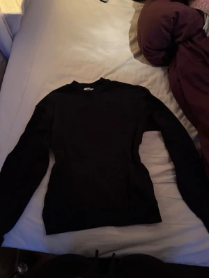 Svart sweatshirt från NA-D - En stilren svart sweatshirt från NA-D i storlek XS. Tröjan har rund hals, långa ärmar och ribbade muddar vid ärmslut och nederkant. Perfekt för dig som gillar enkel och klassisk design. Materialet känns mjukt och bekvämt mot huden.