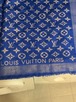Blå Louis Vuitton väst med guldmönster - Säljer en blå väst från Louis Vuitton med ikoniskt guldigt monogrammönster över hela plagget. Västen har en glittrig finish och klassisk design med fransad kant. Perfekt för dig som vill sticka ut och addera lite lyx till din outfit.
