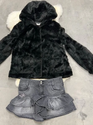 Svart pälsjacka med huva från OVS - Säljer en svart pälsjacka från OVS med mjuk fuskpäls och huva. Jackan har en rak passform och långa ärmar, perfekt för dig som vill ha en mysig och cool look. Enkel design utan synliga knappar eller dragkedja framtill.