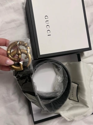  bälte med ormspänne - Säljer ett svart Gucci bälte med ett unikt spänne i antikguld som har en detaljerad orm runt GG-loggan. Bältet är tillverkat i skinn och kommer i originalförpackning med dustbag. Perfekt accessoar för att lyfta din outfit.
