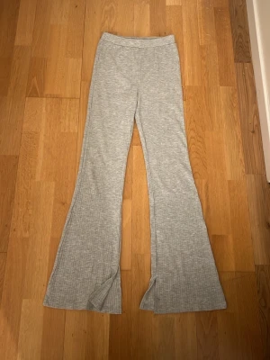 Grå ribbade bootcut-byxor från  Kappahl - Snygga ljusgrå ribbade bootcut-byxor från Kappahl. Byxorna har breda ben och slits vid benslutet. Perfekta för en chill och trendig look. Storlek står ej men skulle säga att dom är xxs/xs