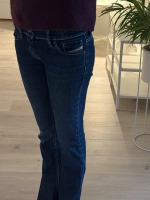 Mörkblå disel jeans  - Snygga mörkblå disel jeans med klassisk femficksdesign och kontrastsömmar. Modellen är bootcut och har låg midja, vilket ger en modern och stilren look. Sydda till bootcut 