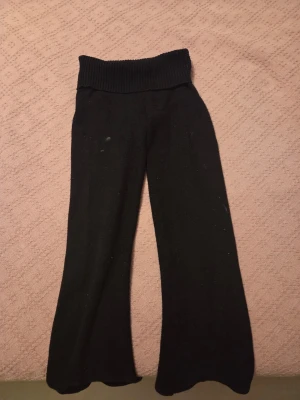 Svarta stickade wide byxor - Svarta stickade byxor med bred ribbad midja och avslappnad passform. Modellen är wide och har ett mjukt, stretchigt material som känns skönt mot huden. Perfekta för chill dagar eller när du vill ha något bekvämt men ändå snyggt. Byxorna är noppriga och har en fläck på framsidan. (Fläcken går säkert att tvätta bort, kan försöka tvätta bort den)