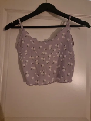 Ljuslila blommig linnetopp - Superfin ljuslila linnetopp med små vita blommor och gröna blad. Toppen har smala axelband och är croppad med vågig kant nertill. Perfekt för varma dagar och ger en söt och somrig vibe.