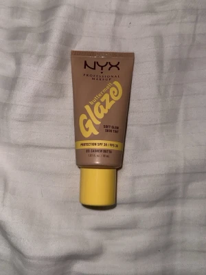 NYX Buttermelt Glaze Skin Tint SPF 30 - NYX Buttermelt Glaze Soft Glow Skin Tint i nyansen 03 Cashew Butta. Lätt färgad foundation med SPF 30, ger en naturlig glow och jämnar ut hudtonen. Innehåller niacinamid, mango och sheasmör. Tub i beige och gult, 30 ml. Endast testad. Nypris 199kr