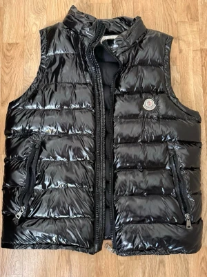 Svart Moncler väst - Säljer en moncler väst som jag knappt använd, den är nästan helt ny och utan skador. Enda problemet är att kedjan går inte att stänga ibland och det går att fixa men annars den är i riktigt bra skick. QR Scan funkar och NFC Scan funkar också.