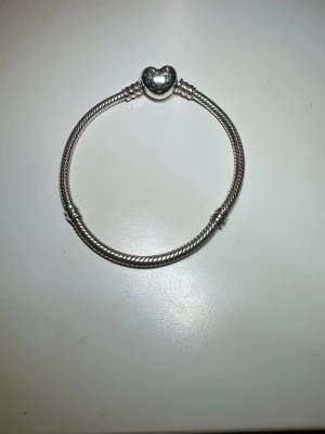 Silver pandora armband - Ett silvrigt Pandora armband med hjärta på. Lite använd men syns inte alls utseendemässigt. Kan lägga till några silver berlocker om man skriver. Budet börjar på 750, kan ändras.