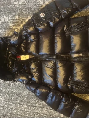 Svart pufferjacka från Moncler - Snygg och tidlös Moncler jacka i klassisk svart med glansig finish. Supervarm men lätt, perfekt för kalla dagar. Bra skick och ikonisk design som aldrig går ur stil. En riktig statement-jacka 🔥Scan funkar på moncler märket inga skador. Pris går att diskuteras privat ⚠️