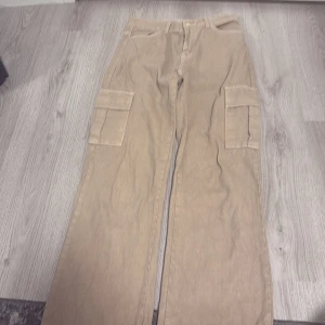 Beiga cargopants med fickor - Säljer ett par beiga cargopants med stora fickor på sidorna och klassisk midja. Byxorna har raka ben och är gjorda i ett mjukt bomullsmaterial. Perfekta för en chill och avslappnad stil. Passar dig som gillar praktiska detaljer och streetwear.