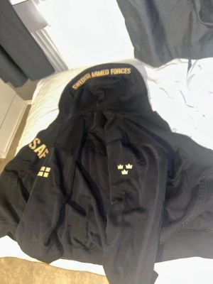 Swedish Armed Forces Zipup Hoodie - Svart/guld Swedish Armed Forces Zipup Hoodie. Väldigt mysig och snygg. Lite för liten så använder aldrig längre, men ganska bra kvalité. Storlek S, står även ”South West Since 1991” i den. Pris kan diskuteras!