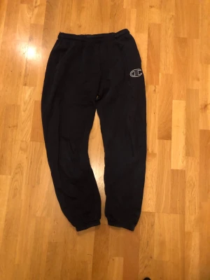 Svarta mjukisbyxor från Champion 2XL 15-16y - Svarta mjukisbyxor från Champion i storlek 2XL. Byxorna har resår i midjan och vid bensluten samt en broderad Champion-logga på benet. Tillverkade i mjukt bomullsmaterial som är skönt att ha på sig. Perfekta för chill eller träning.