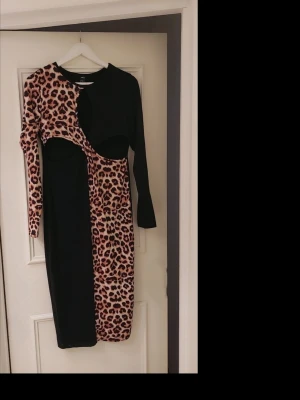 Svart och leopardmönstrad klänning - Unik svart klänning från shein med leopardmönstrade detaljer och asymmetrisk design. Klänningen har lång ärm på ena sidan och cool cut-out vid midjan. Materialet är mjukt och stretchigt, perfekt för dig som vill sticka ut.