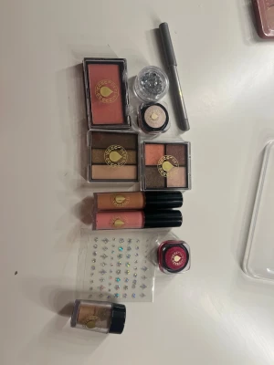 Sminkset med ögonskuggor och läppglans - Säljer ett komplett sminkset från Depend med två paletter ögonskugga i jordnära och varma toner, rouge i persikorosa, två läppglans i nude och rosa, eyeliner i silver, lösglitter, shimmerkräm, rött läppbalsam och dekorstenar. Perfekt för att skapa kreativa looks.