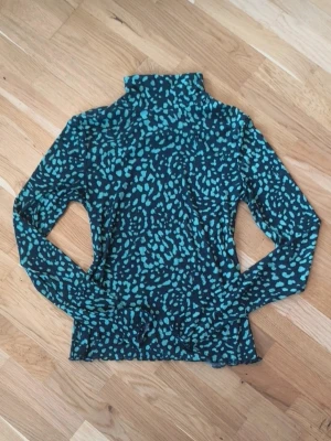 Svart tröja med grönt leopardmönster - Svart polotröja från Lindex i storlek M med grönt leopardmönster.