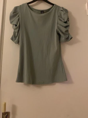 Grön ribbad topp med puffärm Shein - Säljer en grön ribbad topp från Shein i storlek XS. Toppen har korta puffärmar som ger en trendig look och är tillverkad i ett mjukt, stretchigt material. Perfekt för dig som gillar stilrena men ändå unika detaljer.