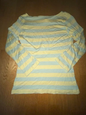 Randig långärmad t-shirt från H&M - Snygg långärmad t-shirt från H&M i storlek S. Tröjan har breda horisontella ränder i ljusblått/ljusgrönt och ljusgult, med en klassisk rund hals. Tillverkad i mjuk bomull som är skön mot huden. Perfekt för dig som gillar en chill och färgglad stil.