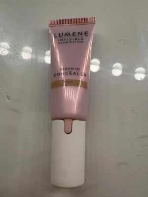 Lumene Serum Concealer Tan - Lumene Invisible Illumination Serum Concealer i färgen Tan. Tuben är ljusrosa med vit botten och har en metallapplikator för smidig applicering under ögonen. Konsistensen är lätt och flytande, perfekt för att täcka mörka ringar och ojämnheter. Öppnad men nästan ny