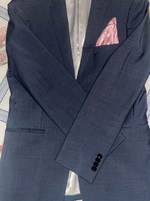 Marinblå kavaj från Esprit - Snygg marinblå kavaj från Esprit med två knappar framtill och fyra dekorativa knappar vid ärmslutet. Kavajen har en klassisk passform och är fodrad med ljusgrått tyg. Bröstfickan är stylad med en ljusrosa paisleymönstrad näsduk för extra stilpoäng.