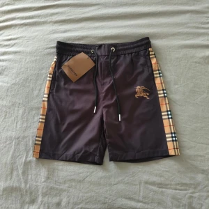 Burberry shorts - Snygga Burberry shorts i marinblå med klassiska rutor på sidorna. Märkta som XL men passar mer som M/L enligt min bedömning. Helt oanvända och i nyskick.