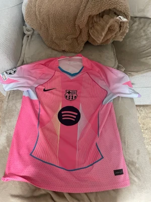 Barça Lamine Yamal rosa matchtröja, L/XL - Säljer en FC Barcelona matchtröja med Lamine Yamal och nummer 10 på ryggen. Tröjan är rosa med vita och ljuslila detaljer, tunna vita ränder och blå kant. Nike-logga på bröstet, Spotify sponsor och UEFA Foundation-märke på ärmen. Perfekt för dig som älskar fotboll och Barça. Både tjejer och killar