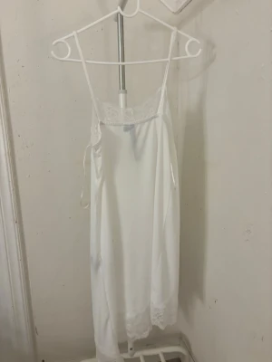 Vit spetskantad nattlinne - Säljer en vit linnetopp med tunna axelband och fina spetsdetaljer vid halsringningen och nederkanten. Toppen har en rak och loose passform, perfekt för sommarens varma dagar. Materialet känns lätt och luftigt.