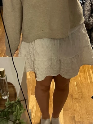 Vit volangkjol från ASOS DESIGN - Säljer en vit kortkjol från ASOS DESIGN med volang och struktur i tyget. Kjolen har en lätt rynkad look och dragkedja i sidan. Perfekt till sommaren! 