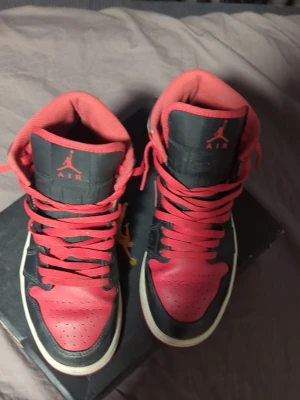 Nike Air Jordan 1 svart/röd sneakers - Säljer ett par Nike Air Jordan 1 sneakers i svart och rött med klassisk high-top design. Skorna har röd snörning, svart och röd skinnöverdel samt vit sula. Ikoniska Jordan-loggan syns på sidan och tungan. Perfekt för dig som vill ha en snygg och sportig look.