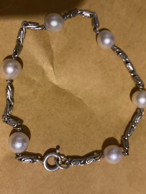 Silver armband med pärlor - Bilderna visar ett pärlarmband med silverfärgade länkar och vita pärlor.