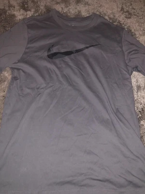 Svart Nike Dri-Fit t-shirt M - Nike Dri-Fit t-shirt i svart med klassisk Swoosh-logga på bröstet. T-shirten är kortärmad och har en rund hals. Materialet är polyester som andas och håller dig torr. Perfekt för dig som gillar sportig och clean stil.