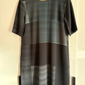 Svart rutig kortklänning Tiger of Sweden - Kort klänning från Tiger of Sweden i nyanser av grått och grönt med diskret rutigt mönster. Klänningen har rund hals, korta ärmar och en slits i ryggen. Materialet är mjukt och känns som polyester, vilket ger ett snyggt fall. Klänningen är aldrig använd. Det står storlek 42 på lappen, men jag skulle säga att den är mer motsvarande medium. 