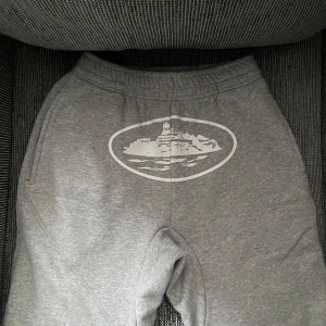 Grå mjukisbyxor med tryck - Grå mjukisbyxor med elastisk midja och sidofickor. Byxorna har ett stort vitt tryck framtill med motiv av en båt i oval ram. Perfekta för chill dagar eller när du vill vara bekväm. Materialet är mjukt och skönt bomullstyg.