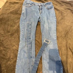 Ljusblå jeans med bälte från NA-KD - Ljusblå jeans från NA-KD i storlek 36, tillverkade i klassiskt denimtyg. Modellen har raka ben och medföljande matchande jeansbälte med metallspänne. OBS trasiga nertill (endast baksida) pga dem varit lite för långa, lite urtvättade också.