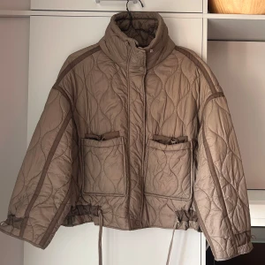 Quiltad beige jacka från Zara - Quiltad beige jacka från Zara med hög krage, två stora fickor framtill och dragsko i midjan samt ärmarna. Passar både till vardags och på kvällen. Den är large men skulle säga att den passar s/m också eftersom man kan dra åt den i midjan och ärmarna för annan passform. 