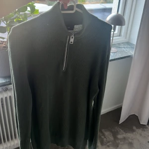 Mörkgrön stickad half zip-tröja H&M - Säljer en mörkgrön stickad tröja från H&M med slim fit-passform. Tröjan har hög krage och en snygg half zip-dragkedja framtill. Perfekt för dig som gillar stilrena och enkla plagg med en modern touch.