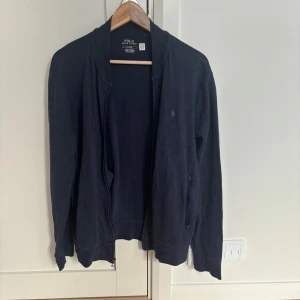 Mörkblå kofta från Polo Ralph Lauren - Mörkblå kofta från Polo Ralph Lauren med dragkedja framtill och diskret logga på bröstet. Långärmad modell i mjuk bomull, perfekt för lager-på-lager. Klassisk och stilren design som funkar till det mesta. Nypris ca 1700 och tröjan är nästan oanvänd! Kom privat för funderingar!🙌