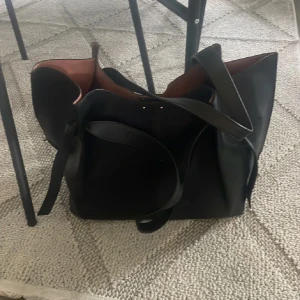 Perfekta skolväskan💕 - Säljer en stor svart axelväska i skinn med brunt innerfoder. Väskan har långa handtag, enkel design och stängs med magnetknapp. Perfekt för dig som vill ha plats för allt du behöver under dagen. Snygg och stilren modell som passar till många outfits.
