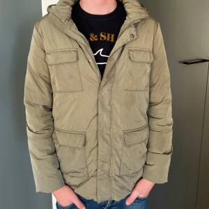Olivgrön massimodutti jacka - Säljer en olivergrön pufferjacka med fyra stora fickor framtill och huva. Jackan har dragkedja och tryckknappar. Perfekt nu när det börjar bli lite kallare. Modellen är 176. Kontakta mig för vidare frågor