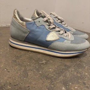 Blå Philippe Model trainers - Snygga sneakers från Philippe Model i blått och silver med vita detaljer. Skorna har snörning och rund tå. Ovandelen är i textil och skinn, med silvriga detaljer vid häl och plös. Perfekta för dig som gillar en sportig och trendig look. Passar perfekt nu till vintern❄️(Pris kan diskuteras) Ny pris 3000. Passar även storlek 41