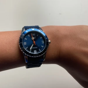 Blå sportig klocka från Regal - Snygg blå klocka från Regal med rund urtavla, blå silikonarmband och detaljer i silver. Urtavlan har tydliga siffror och en orange sekundvisare. Boetten är i rostfritt stål och klockan är vattentålig (3ATM). Perfekt accessoar för en sportig look. Klockans storlek kan justeras just för din storlek.