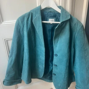 Turkos mockajacka från Cleo - Snygg turkos mockajacka från Cleo med klassisk krage och tre knappar framtill. Jackan har en rak passform och är helfodrad, vilket ger en stilren look 🩵jag är en storlek M och den passar mig 