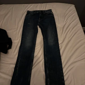 Replay Jacksy blå jeans straight fit - Snygga blå jeans från Replay, modell Jacksy, med klassisk femficksdesign och raka ben. Jeansen har en mörk tvätt med lätt slitna detaljer och tydliga sömmar. Märkespatch bak i midjan och diskret broderi på bakfickorna. Perfekta för en avslappnad stil.
